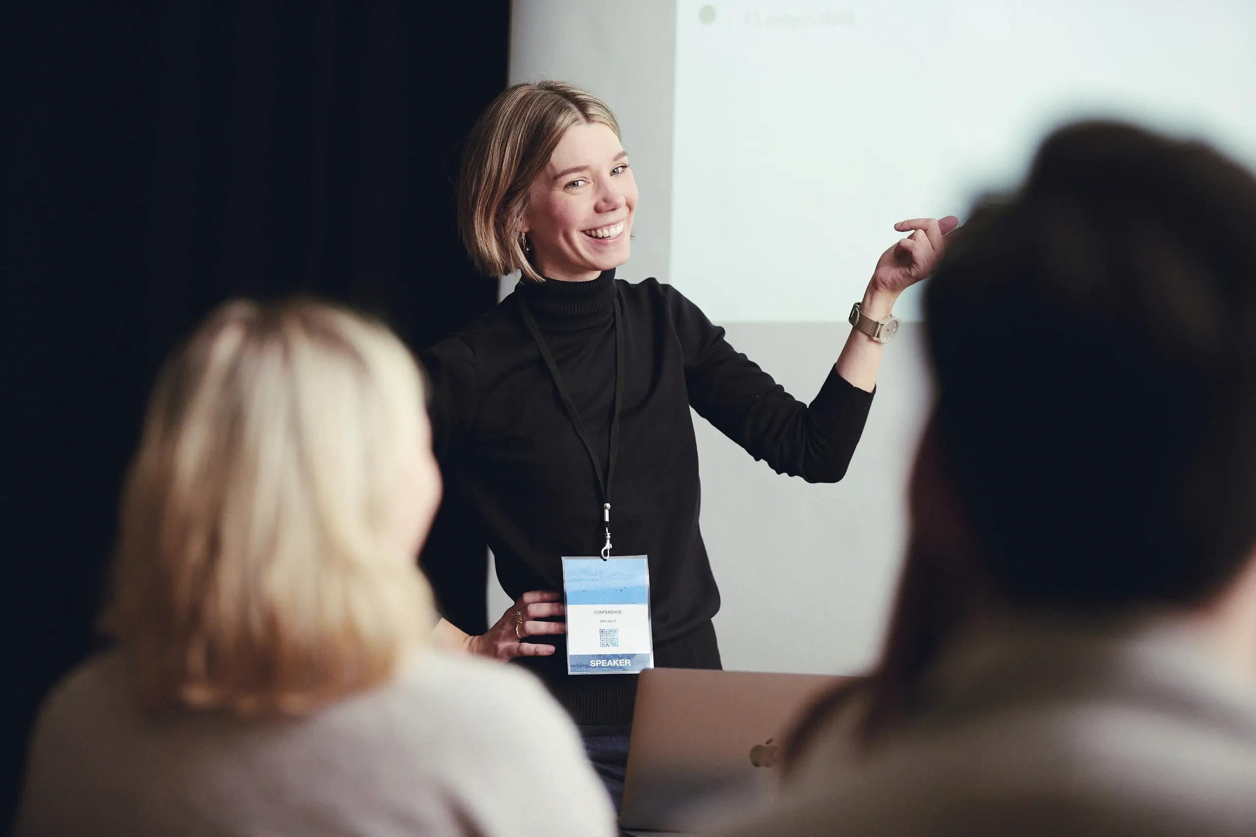 Lina Johnsson, projektledare, ler och pekar åt ett håll medan hon tittar mot personer som sitter ned