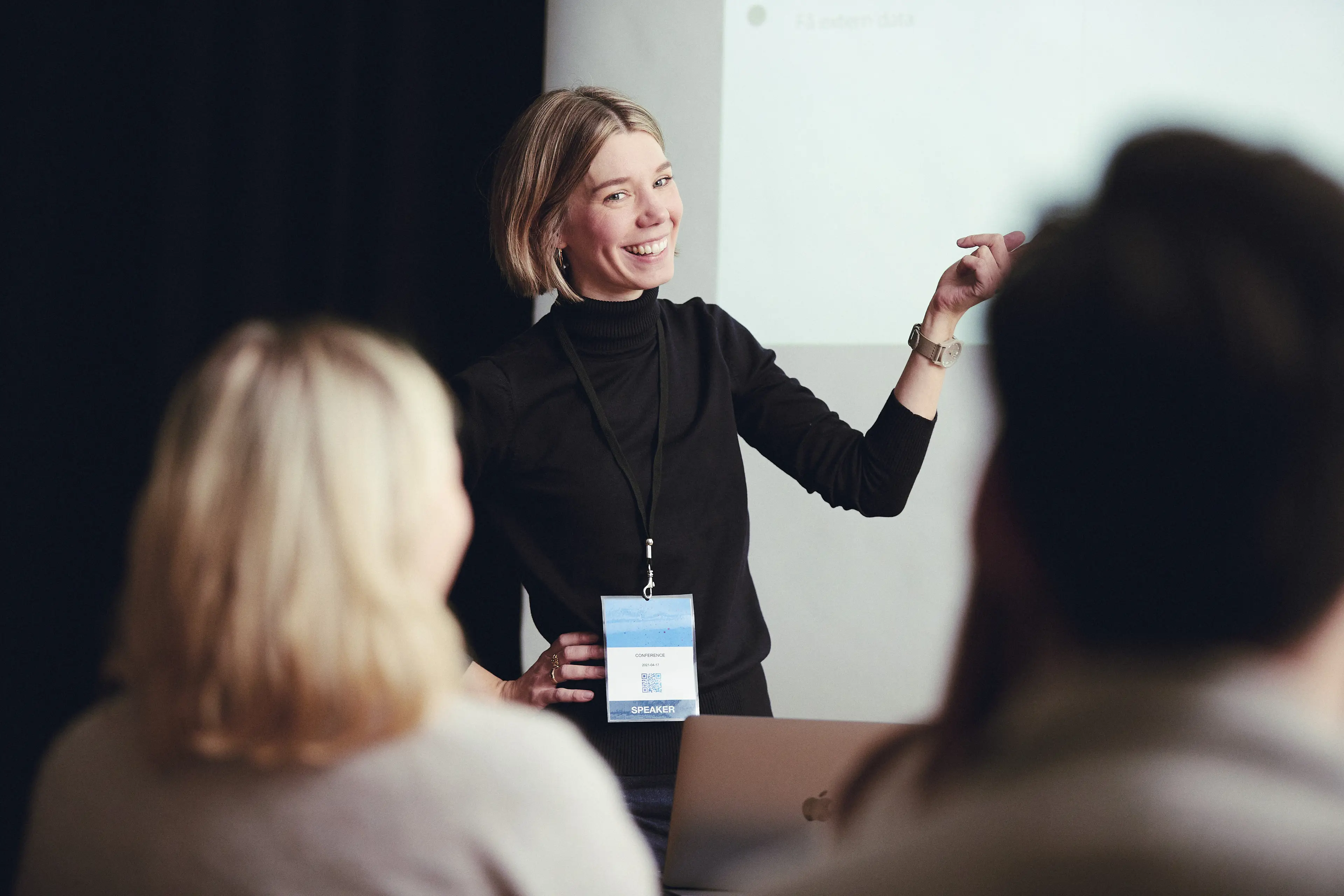 Lina Johnsson, projektledare, ler och pekar åt ett håll medan hon tittar mot personer som sitter ned