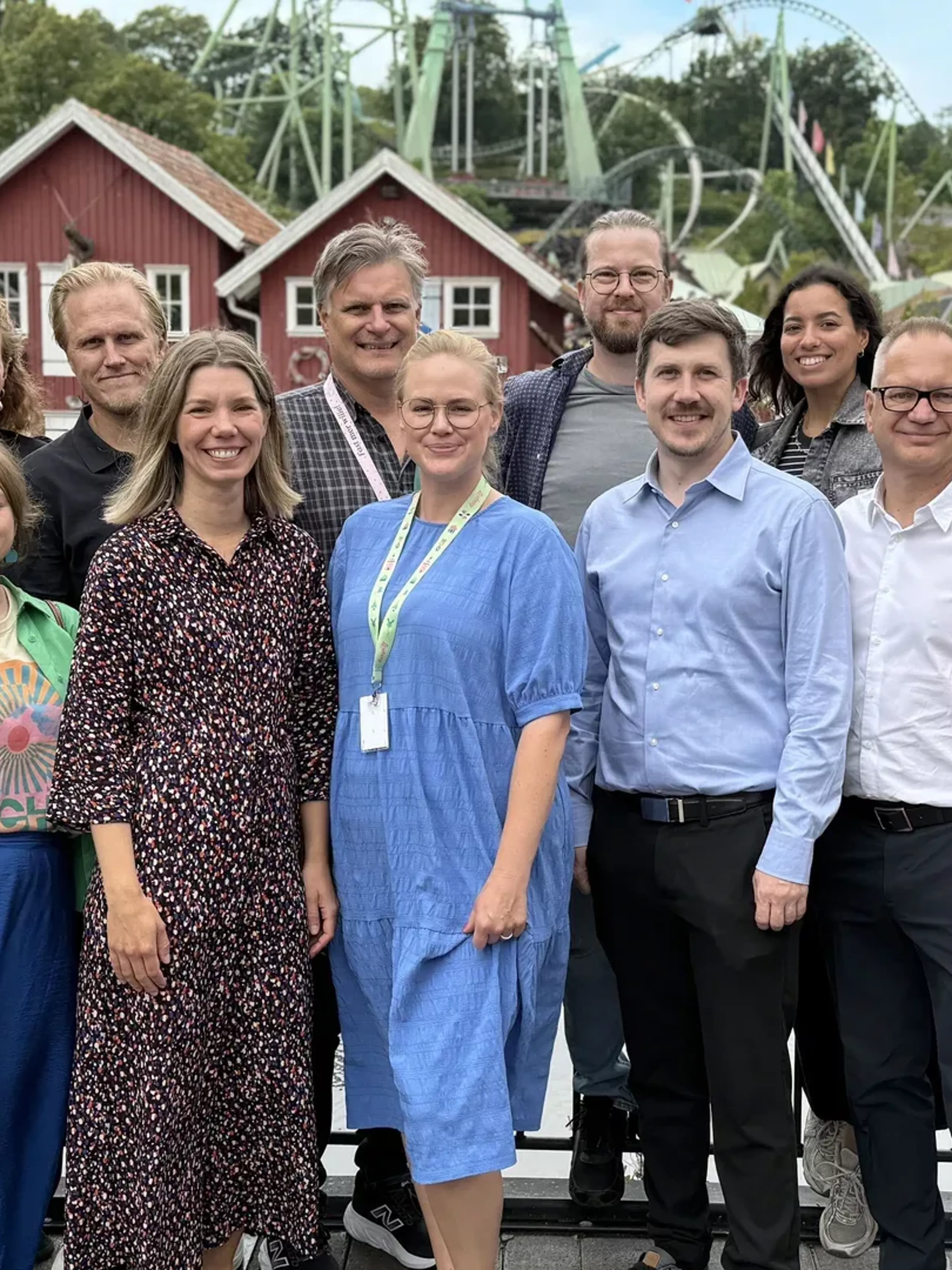 Personer på rad med byggnader och berg-och-dalbanor i bakgrunden