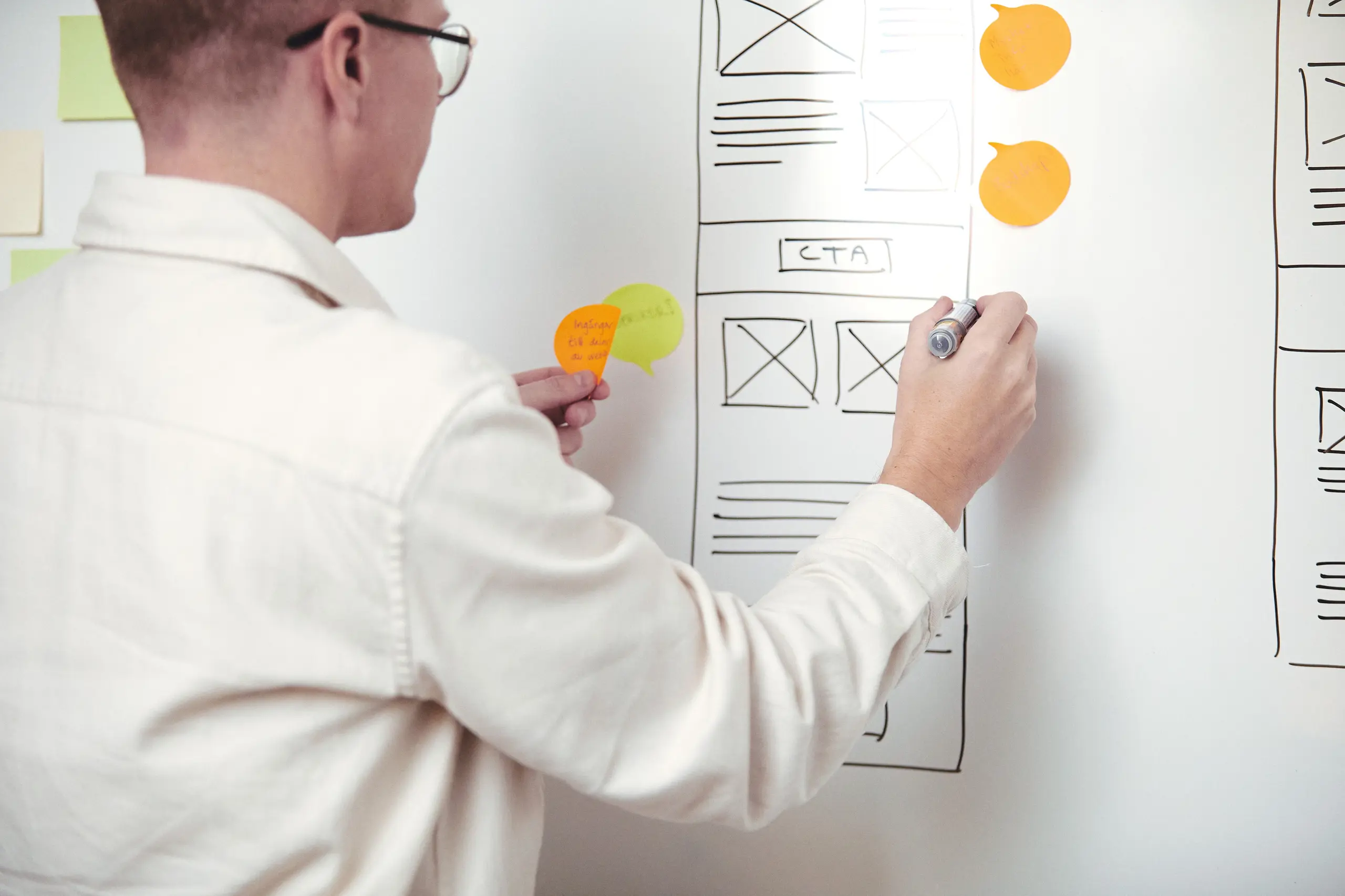 En man står framför en whiteboard med uppritade wireframes och post-its